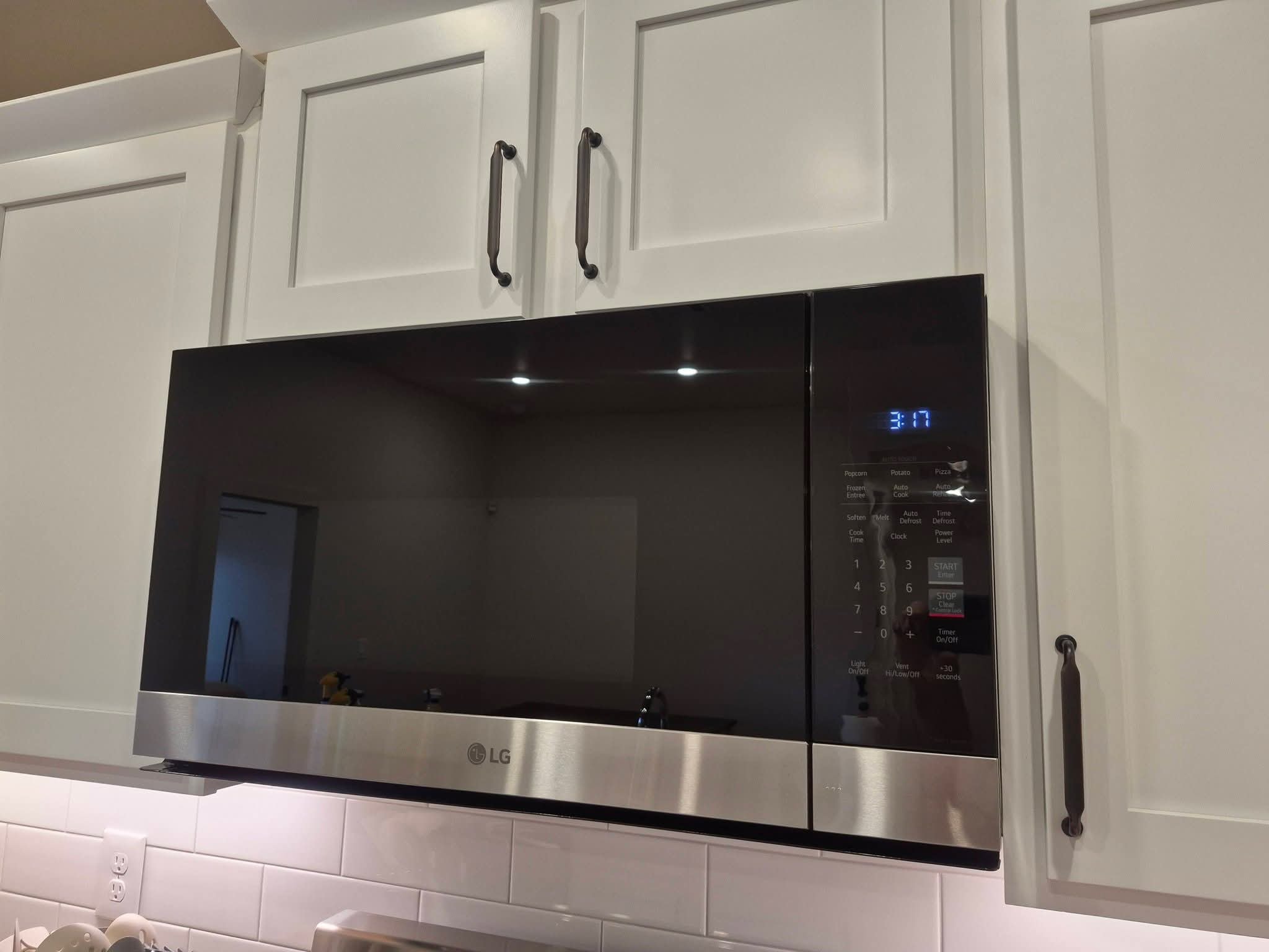 Clean stainless steel microwave above stovetop with white kitchen cabinets